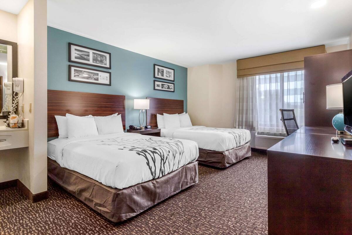 Habitación de hotel con dos camas, un escritorio, un espejo y cuadros en la pared.