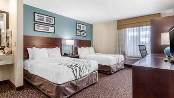 Quarto de hotel com duas camas, uma escrivaninha, um espelho e quadros nas paredes.
