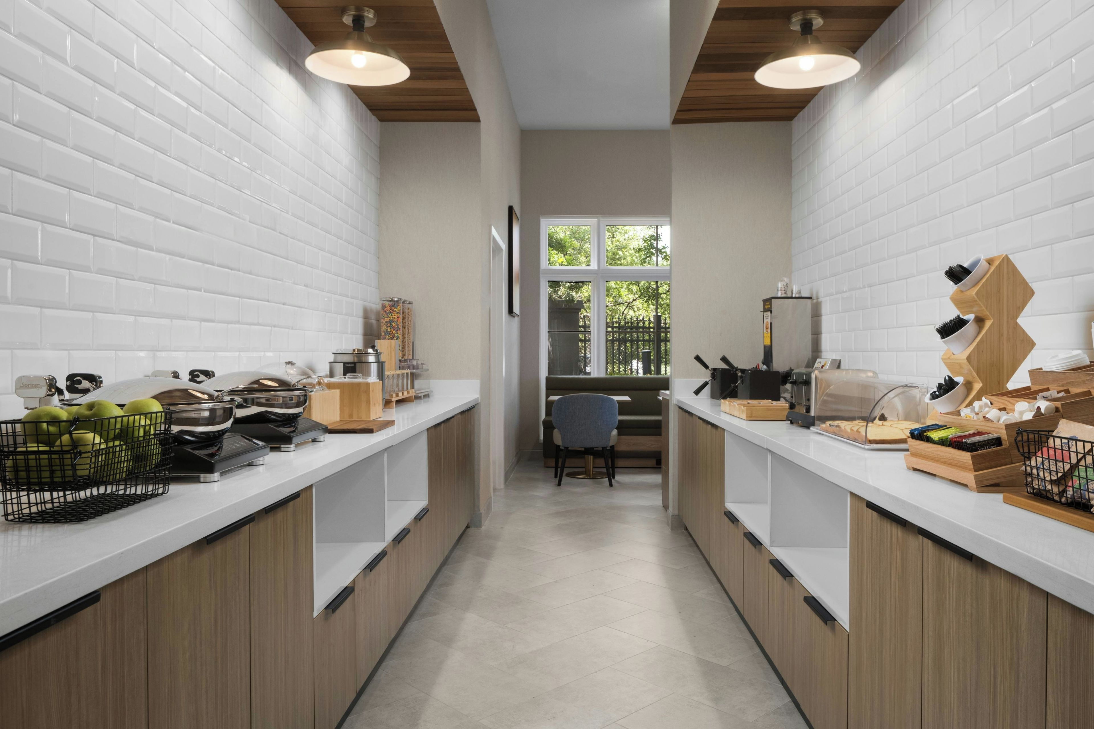 Cozinha estreita com azulejos brancos tipo metrô, armários de madeira e uma janela com vista para o verde lá fora.