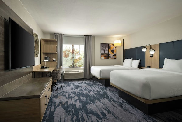 Habitación de hotel con cama, escritorio, silla, televisión y ventana con cortinas.
