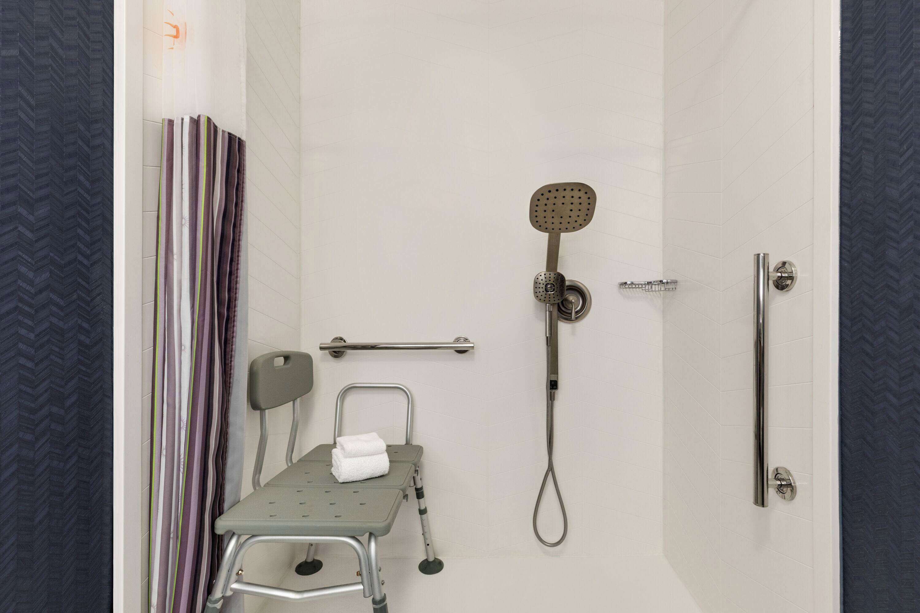 Zona de ducha con cabezal de ducha de mano, barra de apoyo, asiento para ducha y toalla en un organizador de ducha.