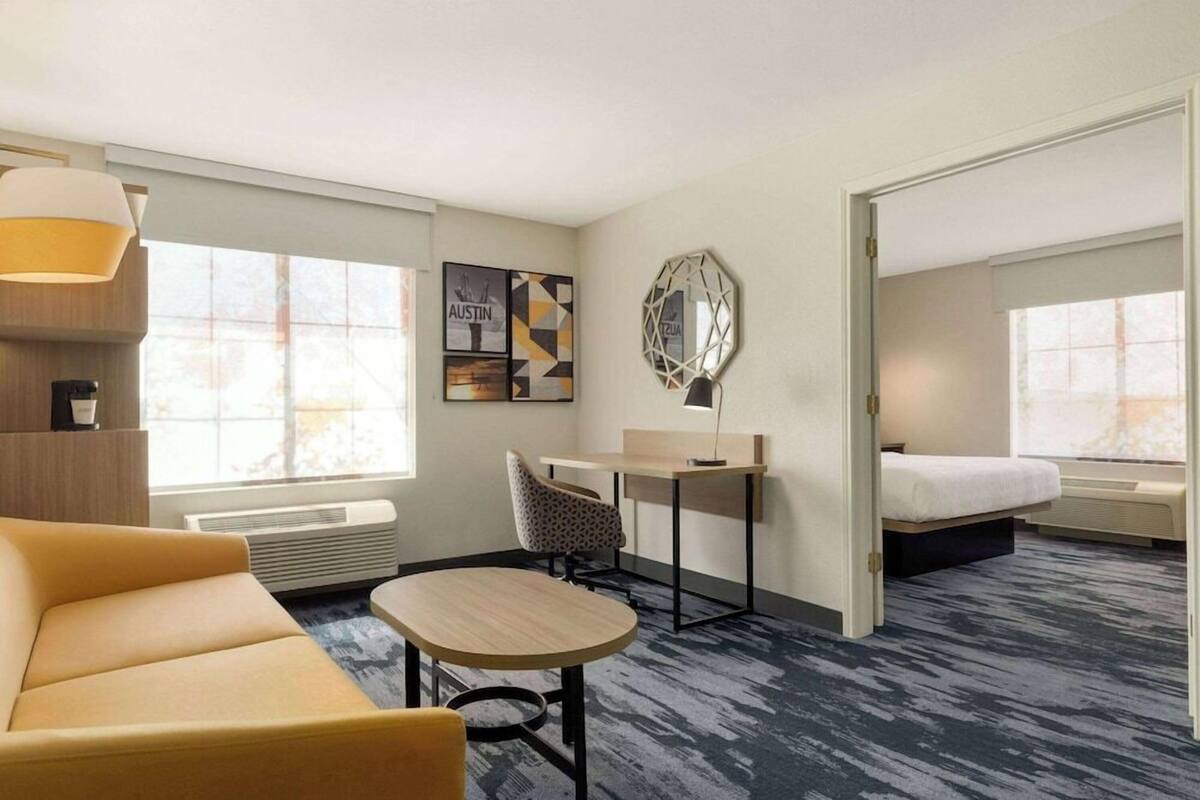 A hotel room with a sofa, a desk, a chair, a bed, and artwork on the walls.