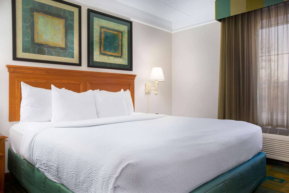 A hotel room with a large bed, a nightstand, a lamp, and two framed artworks on the wall.