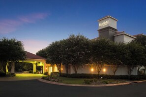 Entrada de un hotel con un cartel que dice 'Fairfield by Marriott', rodeado de árboles y un camino bien iluminado.