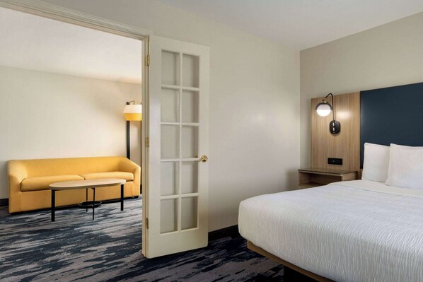 A hotel room with a bed, a sofa, a small table, a nightstand, and a lamp. - Fairfield Inn & Suites by Marriott Austin Southwest (Austin)
