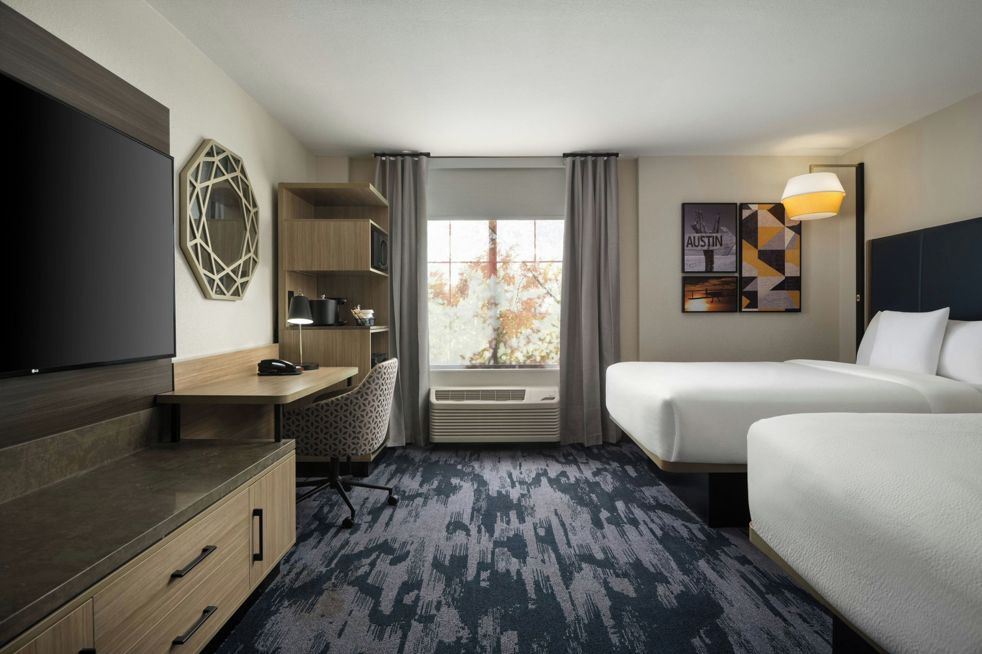 A hotel room with a bed, a desk with a chair, a TV, a bookshelf, and a window with curtains.