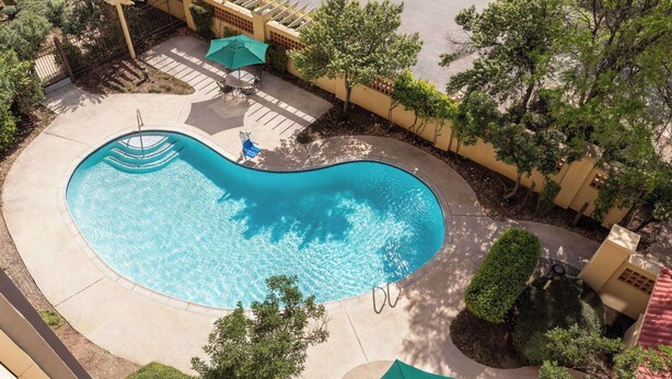 A swimming pool with a curved edge, surrounded by a paved deck, a pergola, and a small patio area with a table and chairs. - Fairfield Inn & Suites by Marriott Austin Southwest (Austin)