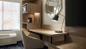 A modern room with a wooden desk, a patterned chair, a wall-mounted mirror, and built-in shelving. - Fairfield Inn & Suites by Marriott Austin Southwest (Austin)