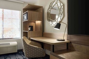 A modern room with a wooden desk, a patterned chair, a wall-mounted mirror, and built-in shelving. - Fairfield Inn & Suites by Marriott Austin Southwest (Austin)