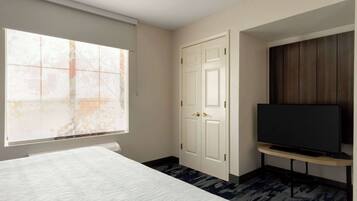 Une chambre d’hôtel avec un lit, un téléviseur posé sur un meuble, une armoire et une fenêtre donnant sur un immeuble.