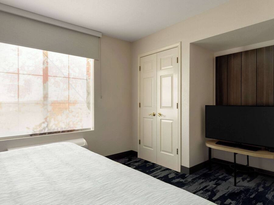 Une chambre d’hôtel avec un lit, un téléviseur posé sur un meuble, une armoire et une fenêtre donnant sur un immeuble.