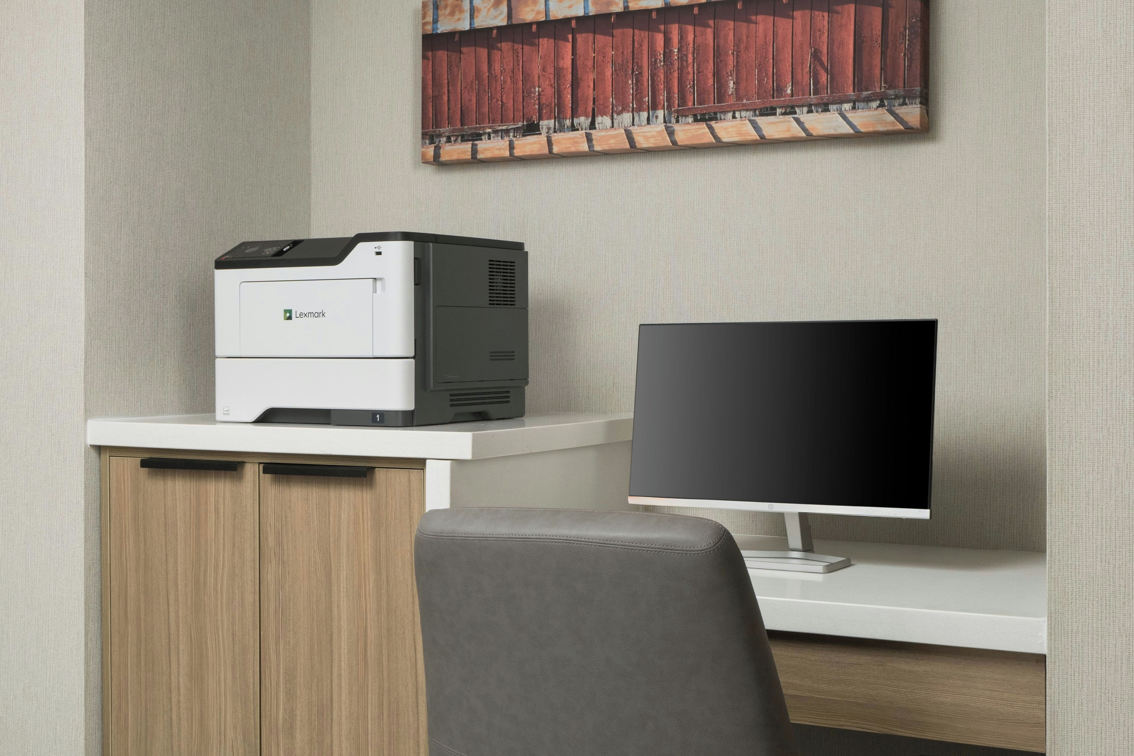 Een moderne werkplek met een printer, een computerbeeldscherm en een bureau.