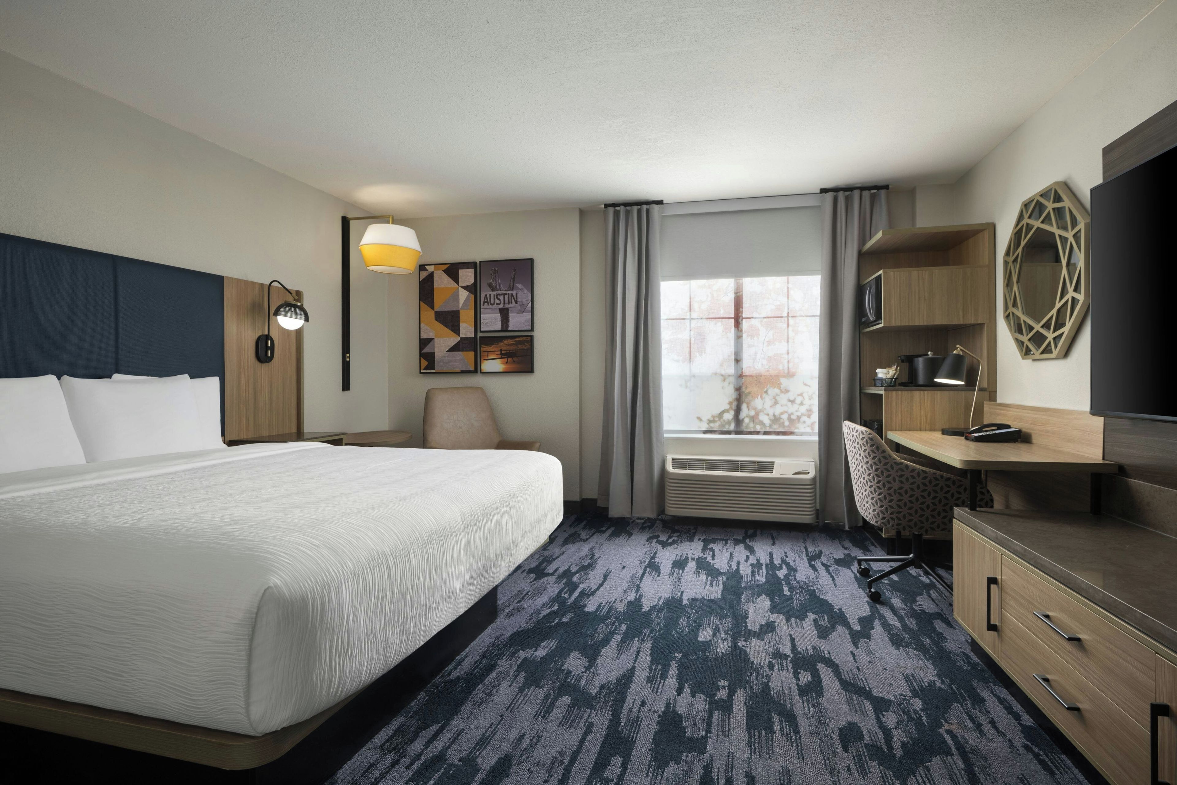 Ein Hotelzimmer mit einem großen Bett, einem Schreibtisch, einem Sessel, einem Fernseher und einem Fenster mit Vorhängen.