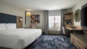 Ein Hotelzimmer mit einem großen Bett, einem Schreibtisch, einem Sessel, einem Fernseher und einem Fenster mit Vorhängen.