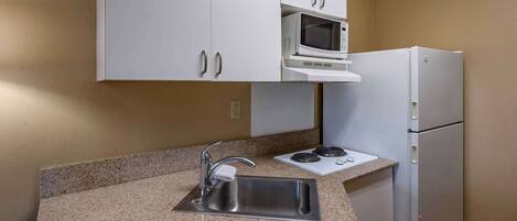 A kitchen with white cabinets, a stainless steel sink, a microwave, a stove, and a refrigerator.