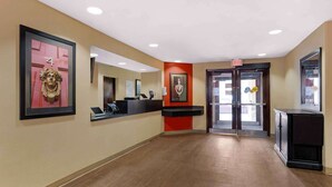 A hotel reception area with a reception desk, a phone, a framed bust on the wall, and a door with an exit sign. - Extended Stay America Suites Houston Med Ctr Greenway Plaza (Houston)