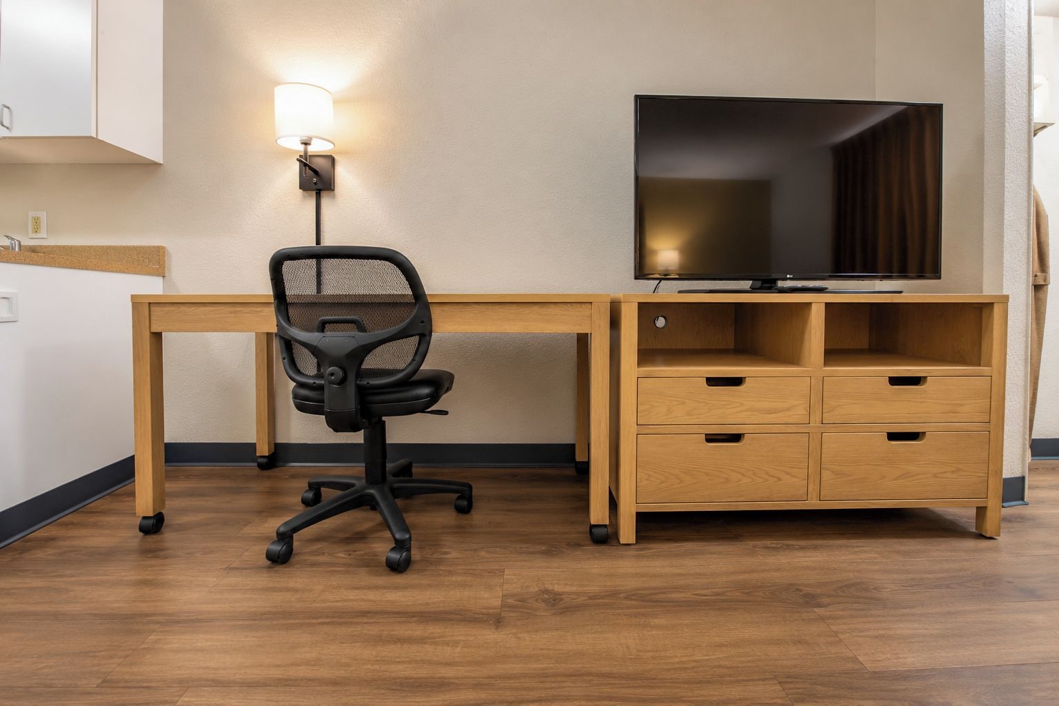 Een moderne kantoorruimte met een bureau, stoel, televisie en inbouwkasten.