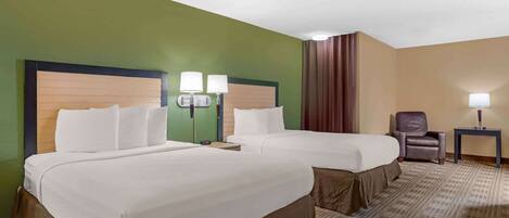 A hotel room with two beds, a chair, a table, and a lamp.