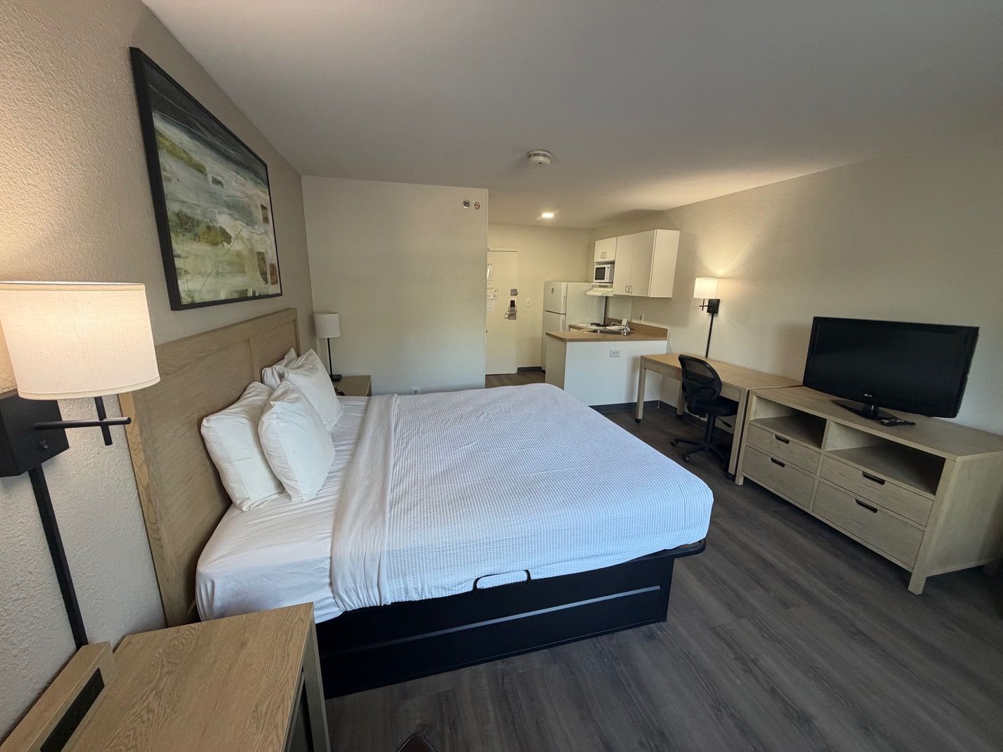A hotel room with a bed, desk, television, and kitchenette.