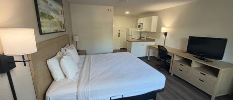 A hotel room with a bed, desk, television, and kitchenette.