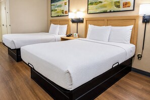 A hotel room with two beds, a wooden headboard, a bedside table with a lamp, and a painting on the wall.
