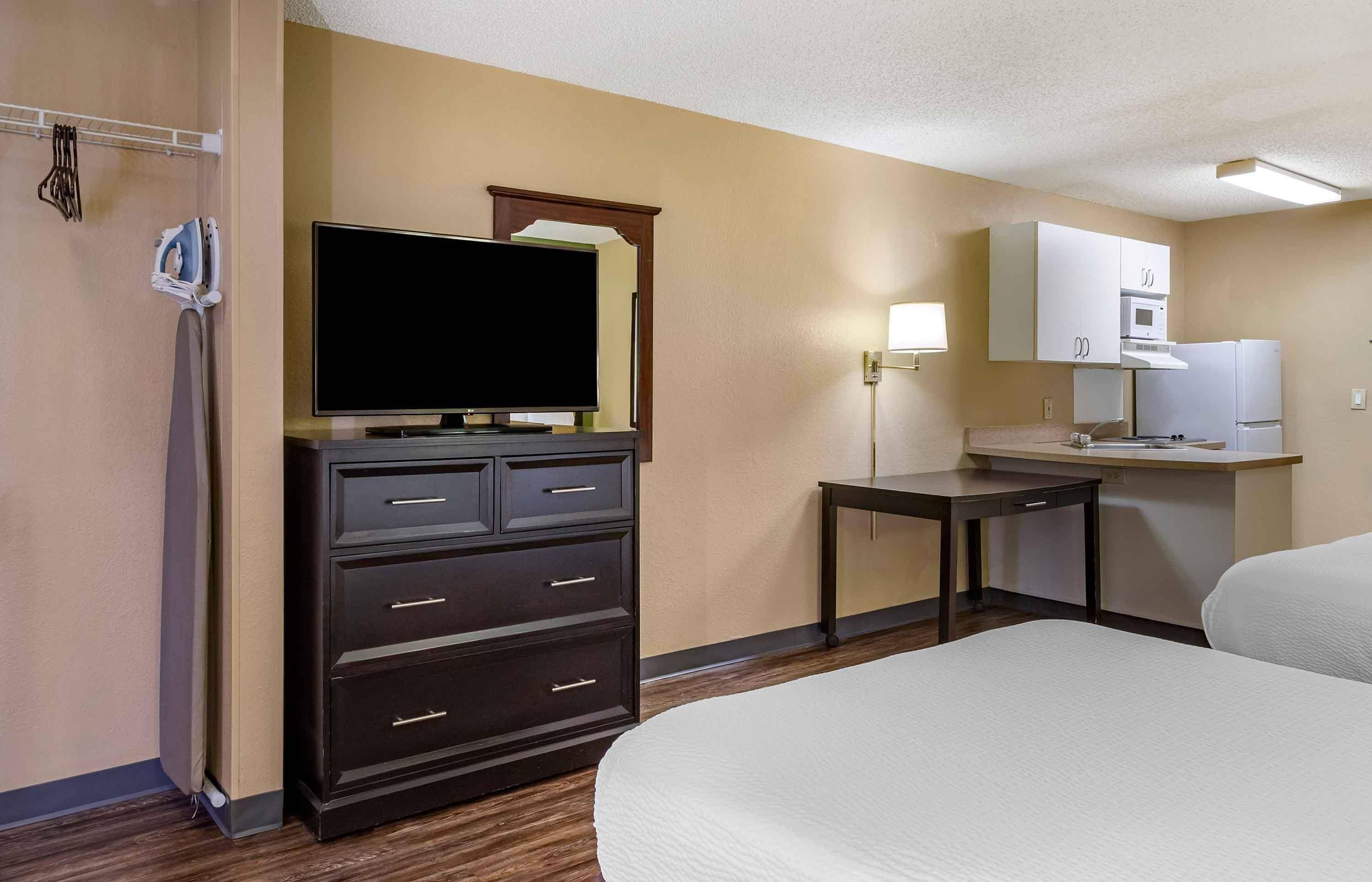 A hotel room with a bed, a dresser, a television, a desk, a microwave, and a refrigerator.
