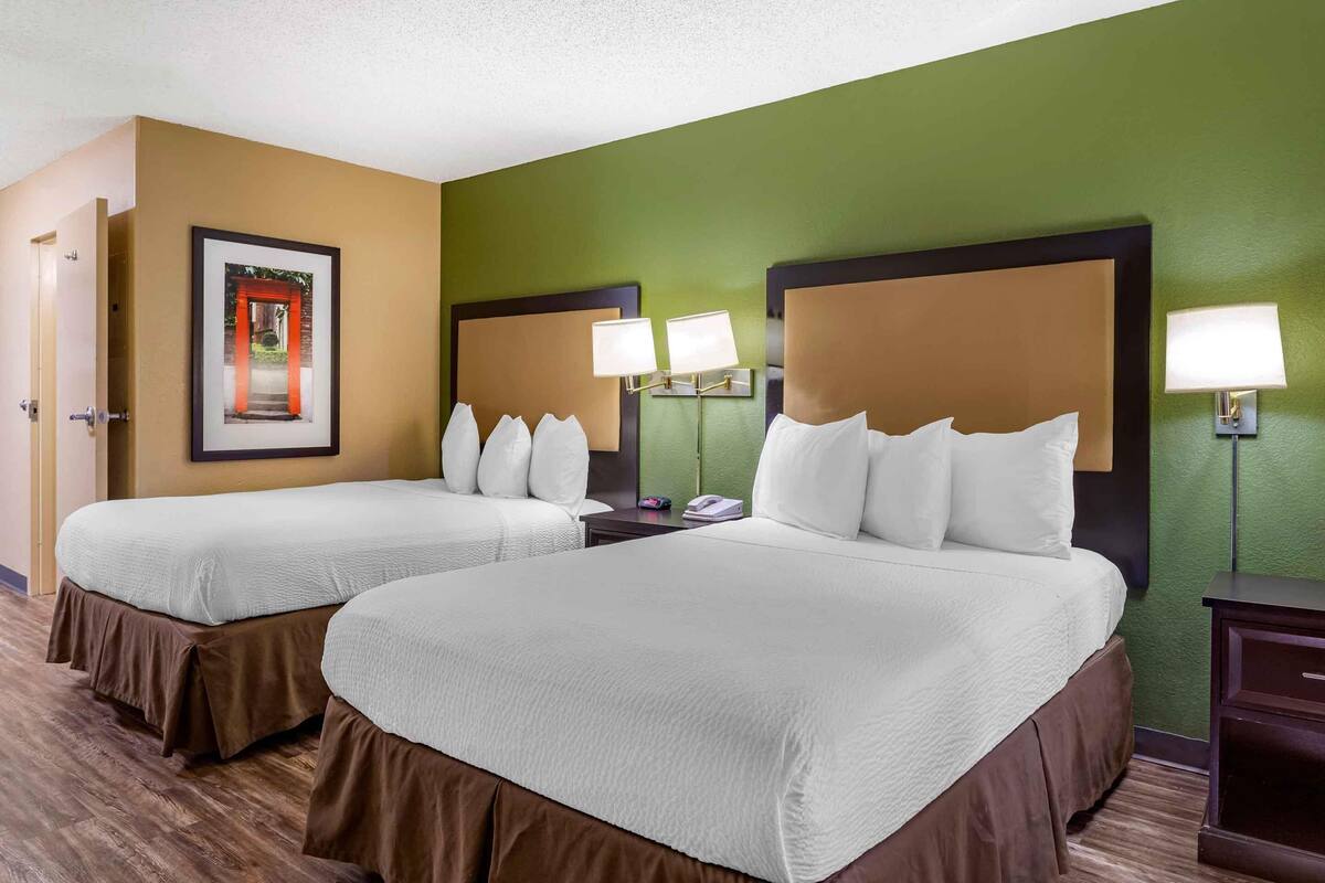 A hotel room with two beds, green walls, and a framed picture of a red archway.