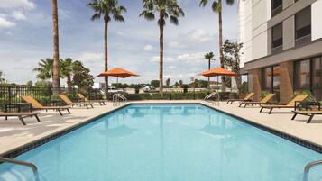 Relax by the pool surrounded by lounge chairs and umbrellas, with a building nearby offering additional amenities.