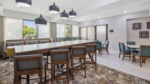 A modern dining area with a long table, bar stools, and pendant lighting. - Hampton Inn Houston-Brookhollow (Houston)