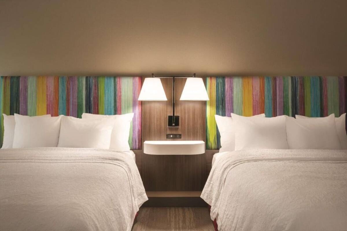A hotel room with two beds, a central sink, and a colorful striped wall.