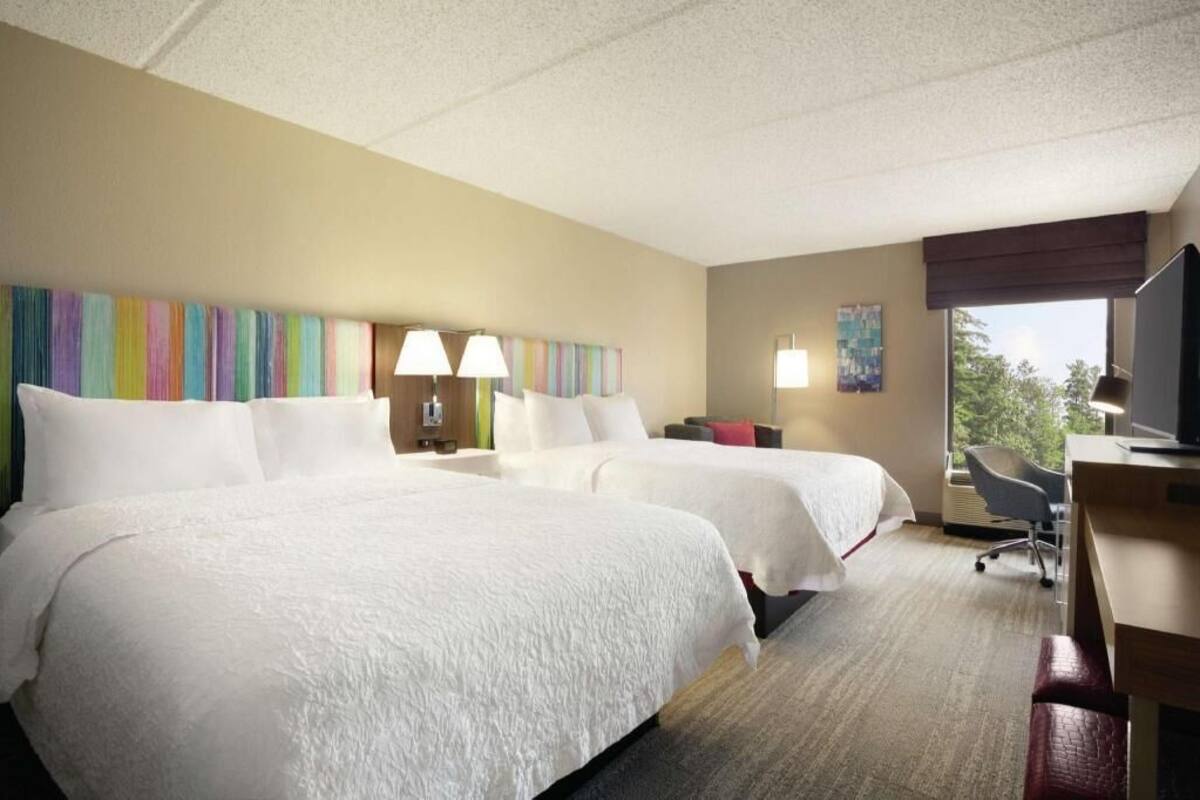 A hotel room with two beds, a desk, a chair, a television, and a window.