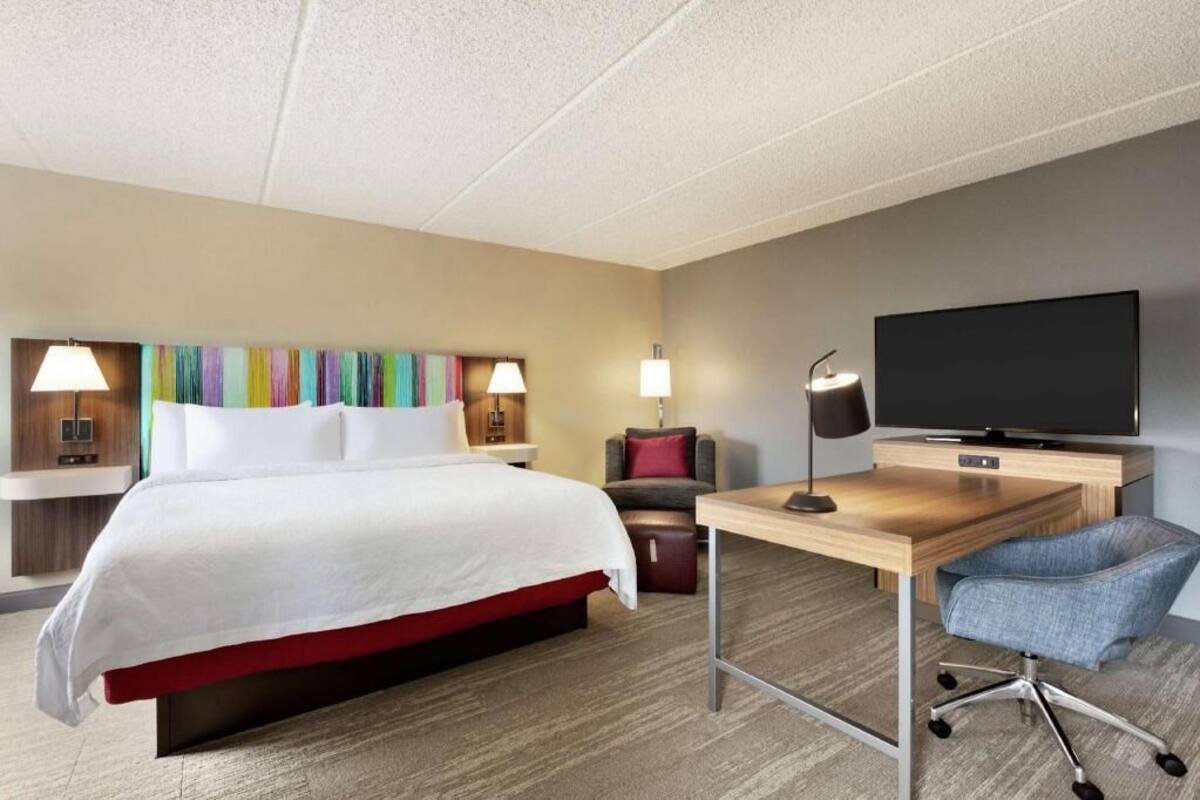 A hotel room with a bed, desk, chair, TV, and colorful artwork on the wall.