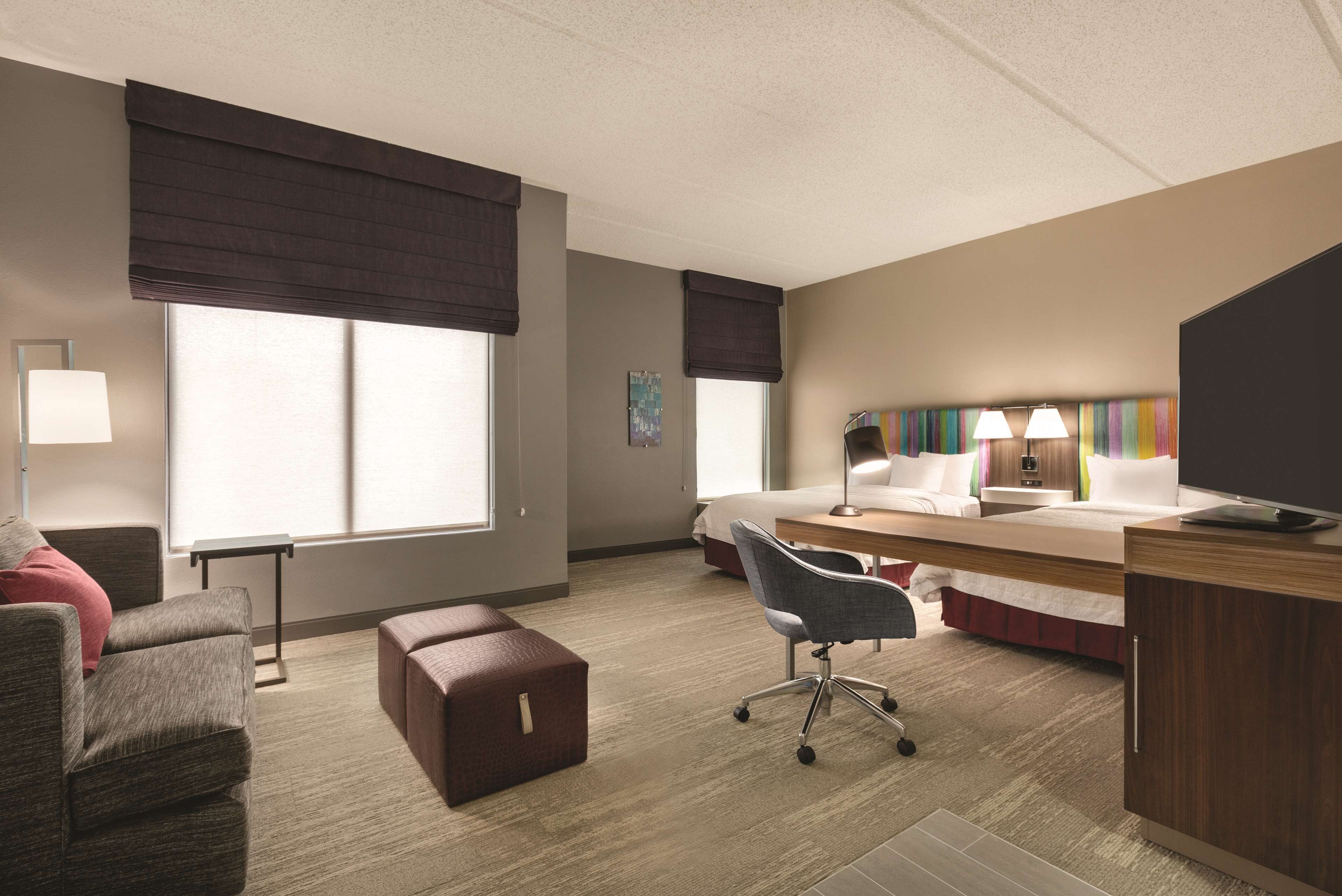 A hotel room with a bed, desk, chair, and a small seating area.