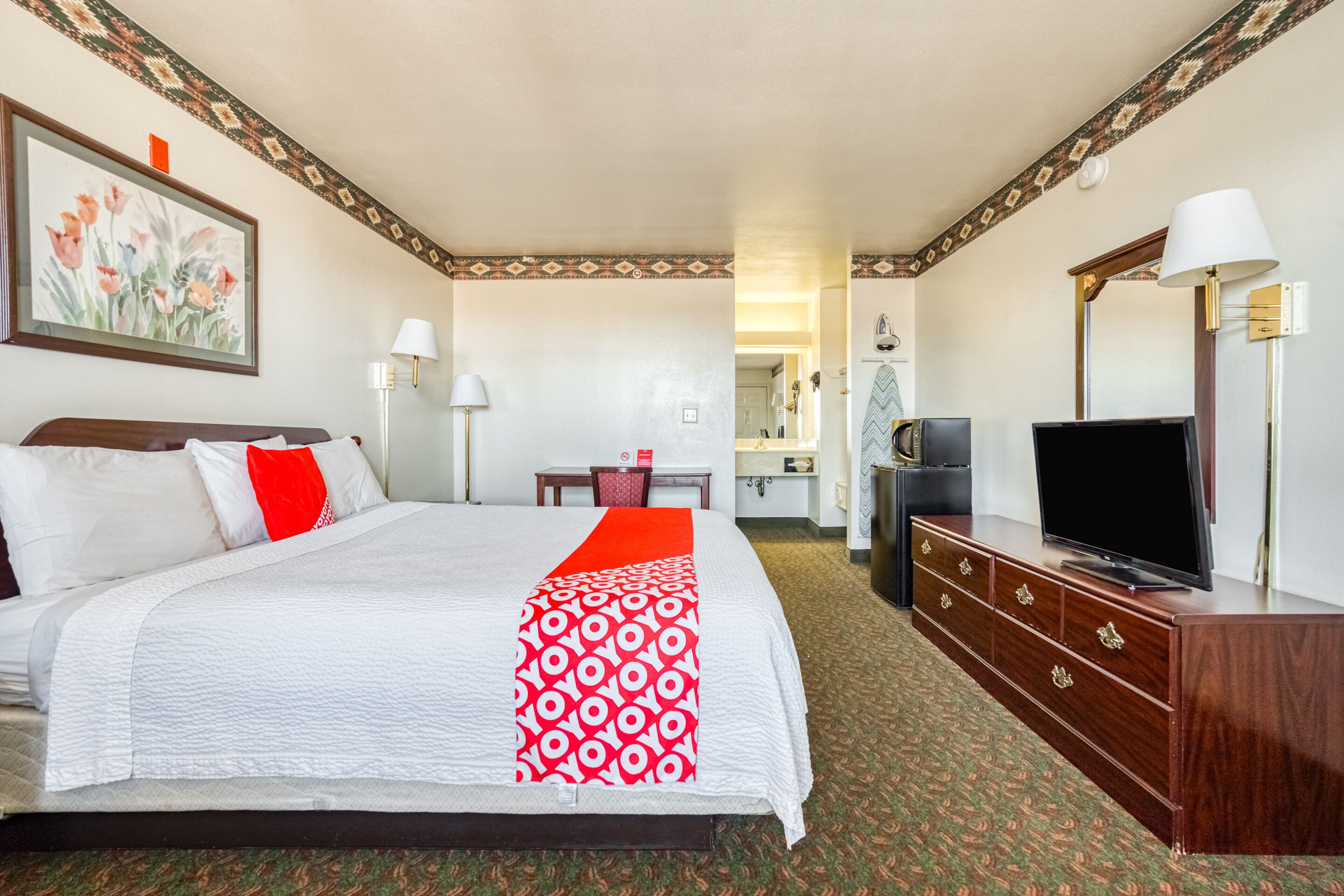 A hotel room with a large bed, a television, a dresser, and a desk with a chair.