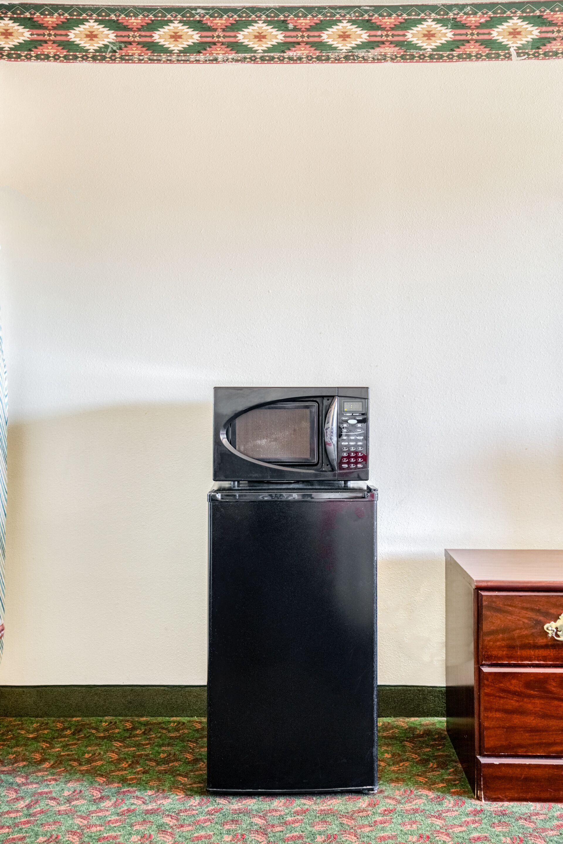 Un refrigerador negro con un microondas encima, un mueble de madera y una alfombra estampada.
