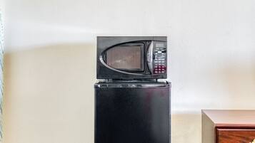 Un refrigerador negro con un microondas encima, un mueble de madera y una alfombra estampada.