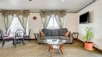 A living room with a sofa, chairs, a glass coffee table, a TV, and a potted plant.