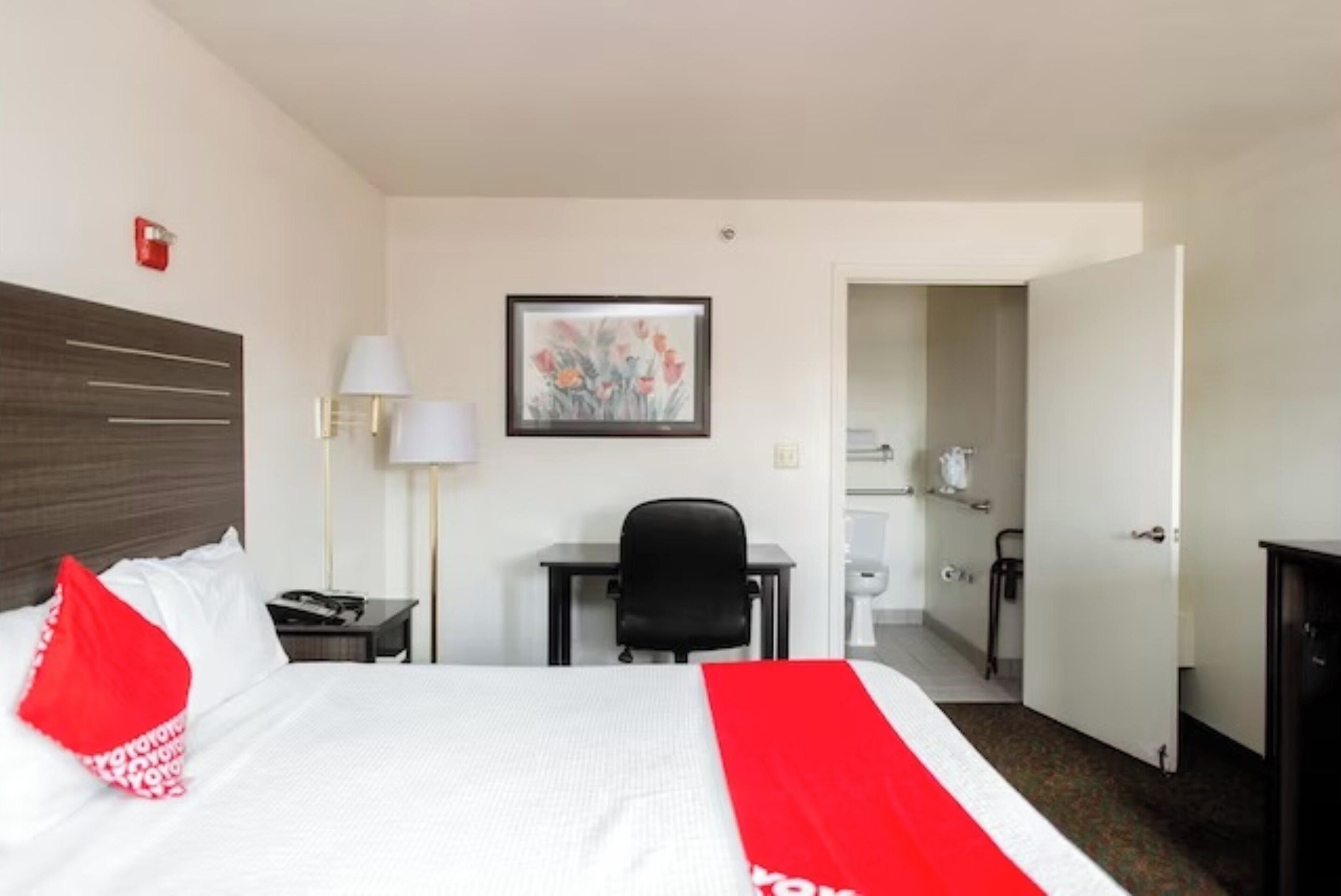 Habitación de hotel con cama, escritorio, silla, lámpara y un cuadro en la pared.