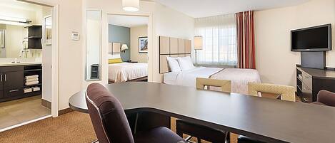A hotel room with a bed, a desk, a chair, a television, and a bathroom visible through an open door.