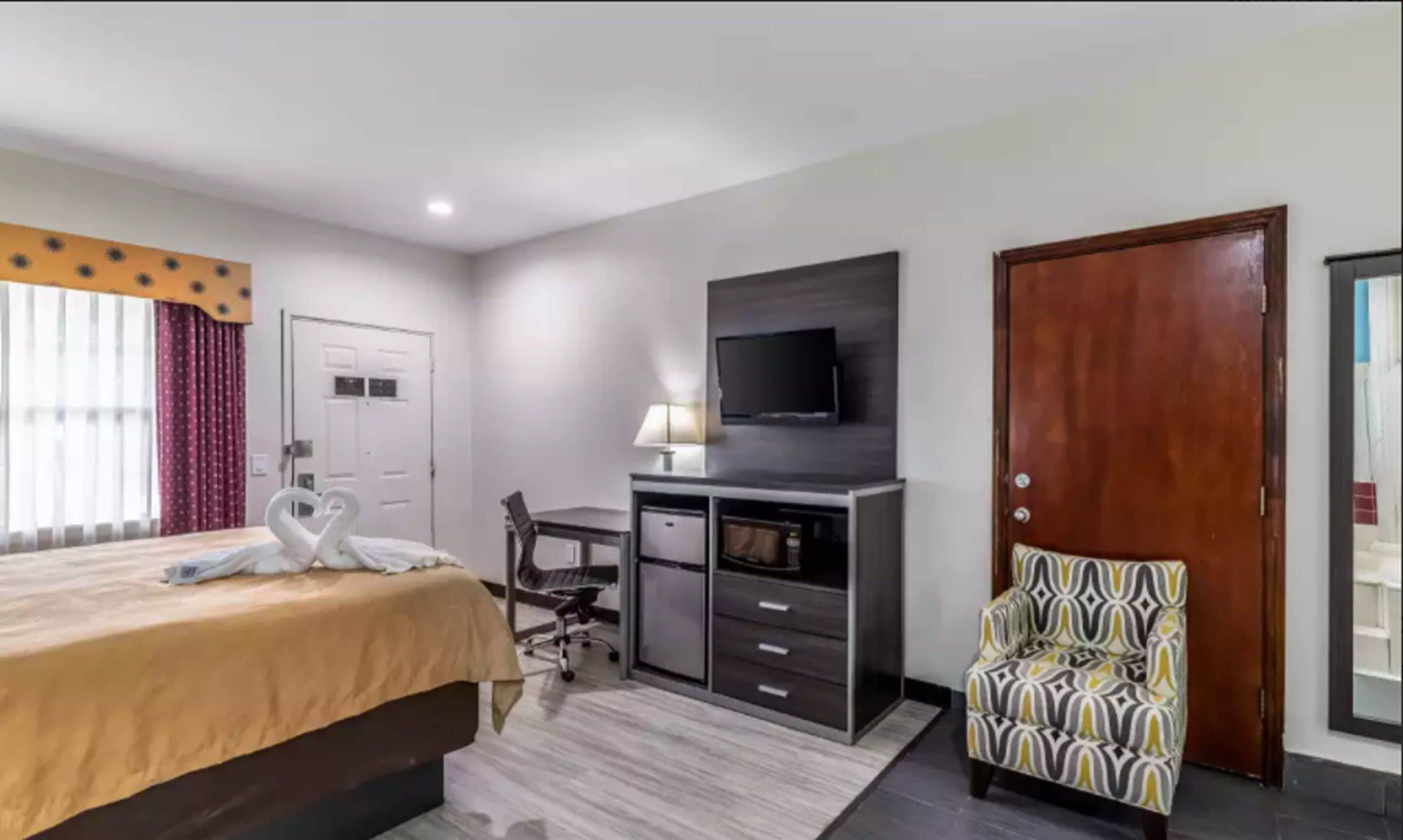 A hotel room with a bed, desk, chair, TV, and a door.