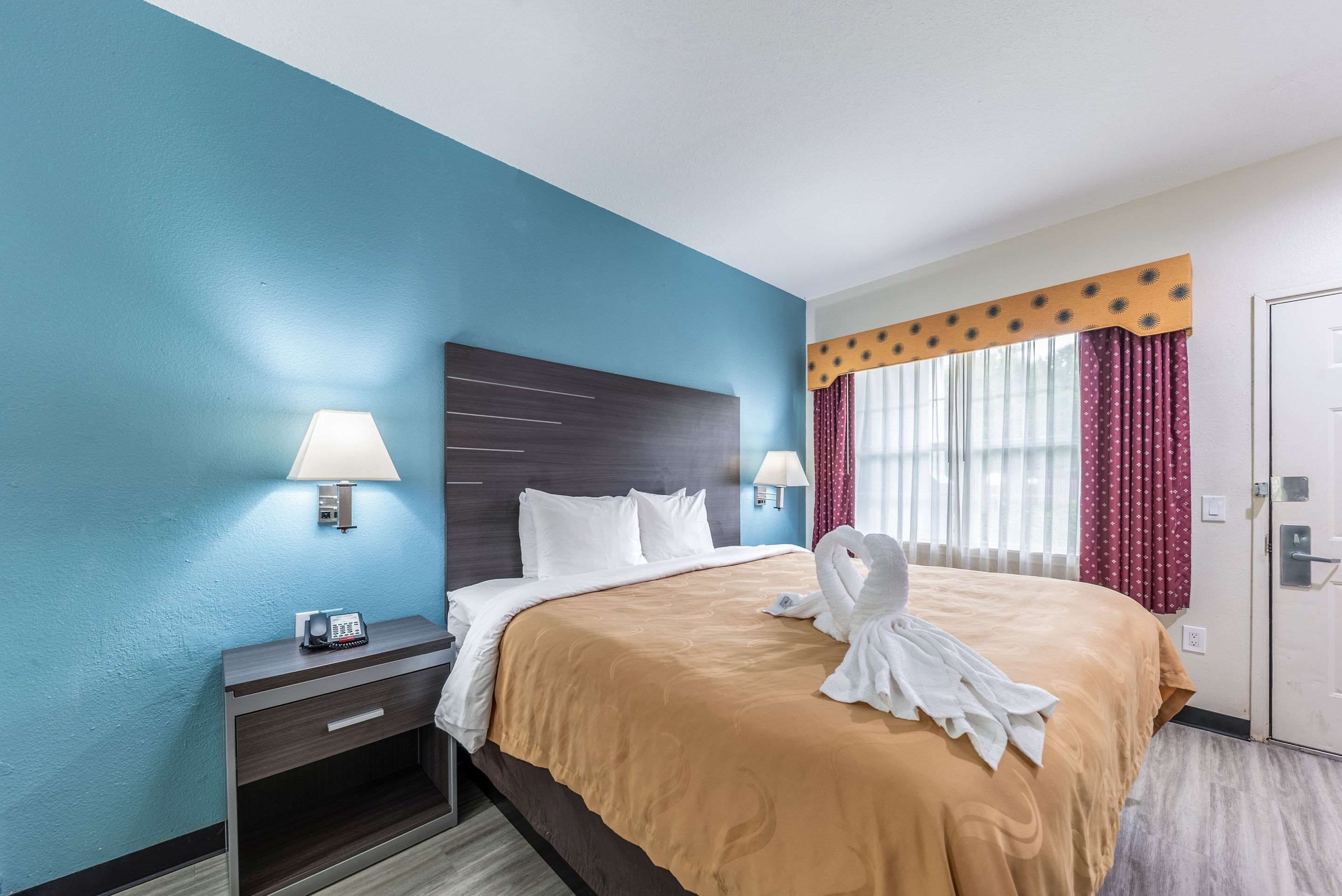 A hotel room with a bed, bedside lamps, a telephone, and a window with curtains.