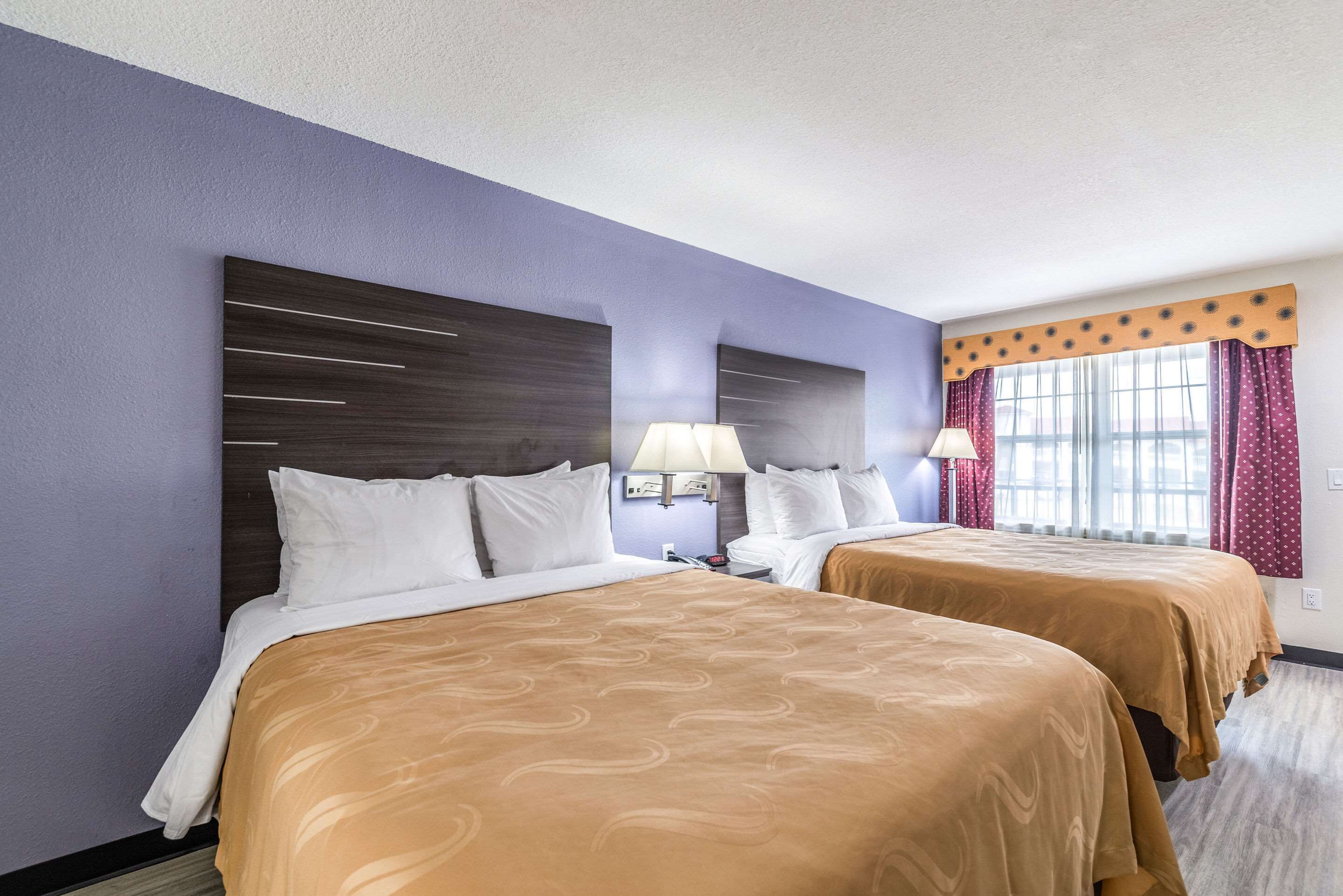 Une chambre d’hôtel avec deux lits, une grande fenêtre avec des rideaux et une tête de lit moderne.