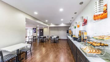 Una cafetería amplia con varias mesas y sillas, un mostrador de buffet con diferentes opciones de comida y un interior moderno y limpio.