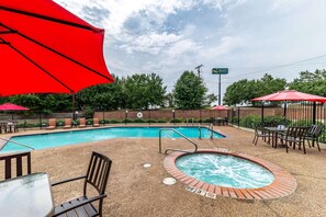 Relax by the pool with comfortable lounge chairs and tables, a hot tub, and a shaded area under a red umbrella.
