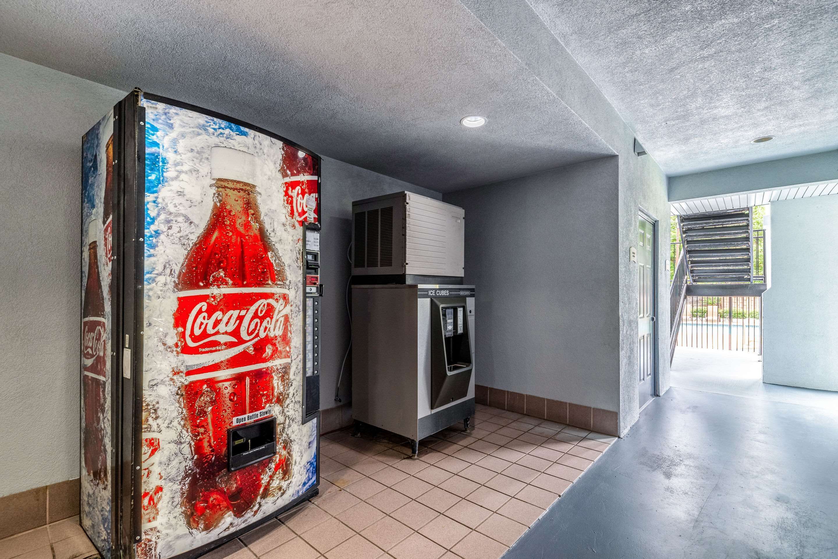 Un couloir avec un distributeur automatique de Coca-Cola, un appareil de climatisation et une porte donnant sur un autre espace.