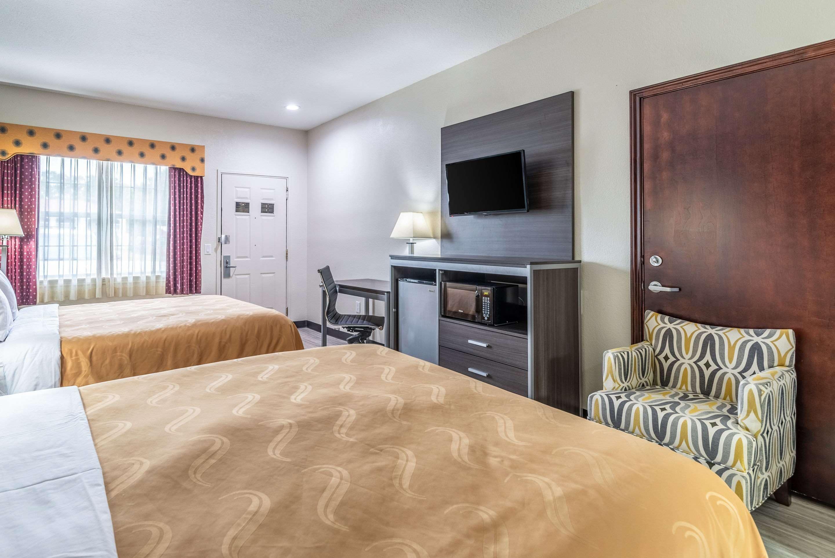 A hotel room with two beds, a TV mounted on the wall, a desk with a chair, and a microwave.