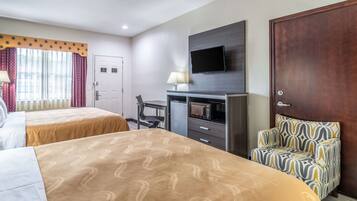 A hotel room with two beds, a TV mounted on the wall, a desk with a chair, and a microwave.