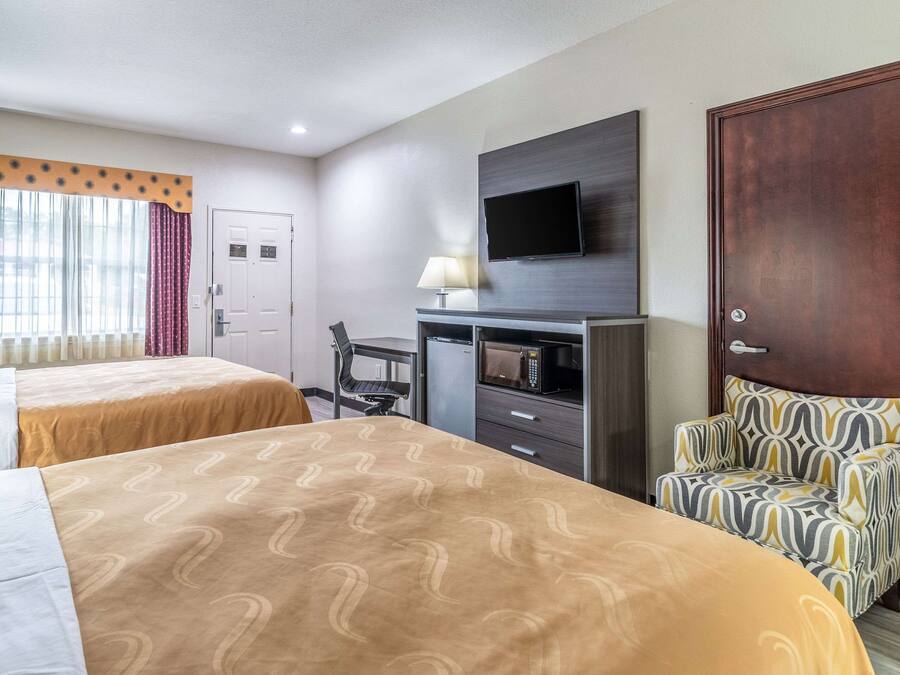 A hotel room with two beds, a TV mounted on the wall, a desk with a chair, and a microwave.