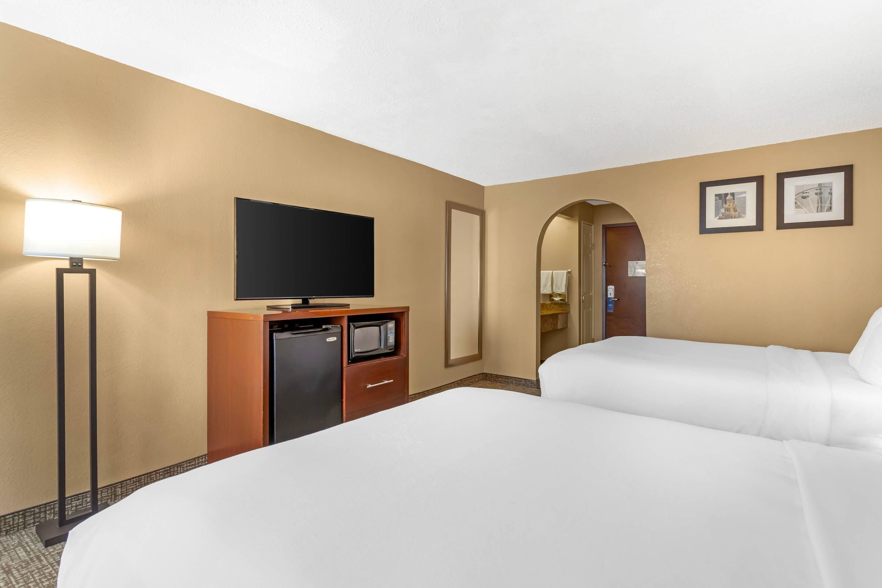A hotel room with two beds, a flat-screen TV, a desk with a microwave, and a lamp.