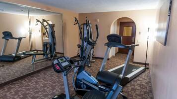 A hotel fitness room with cardio machines, a mirror, and a patterned carpet.